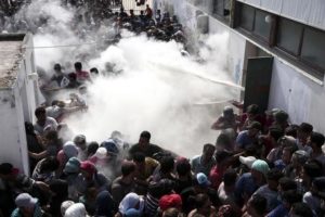 Policemen try to disperse hundreds of migrants by spraying them with fire extinguishers, during a registration procedure which was taking place at the stadium of Kos town, on the southeastern island of Kos, Greece, Tuesday, Aug. 11, 2015. Fights broke out among migrants on the Greek island of Kos Tuesday, where overwhelmed authorities are struggling to contain increasing numbers of people arriving clandestinely on rubber dinghies from the nearby Turkish shore.  (ANSA/AP Photo/Yorgos Karahalis)